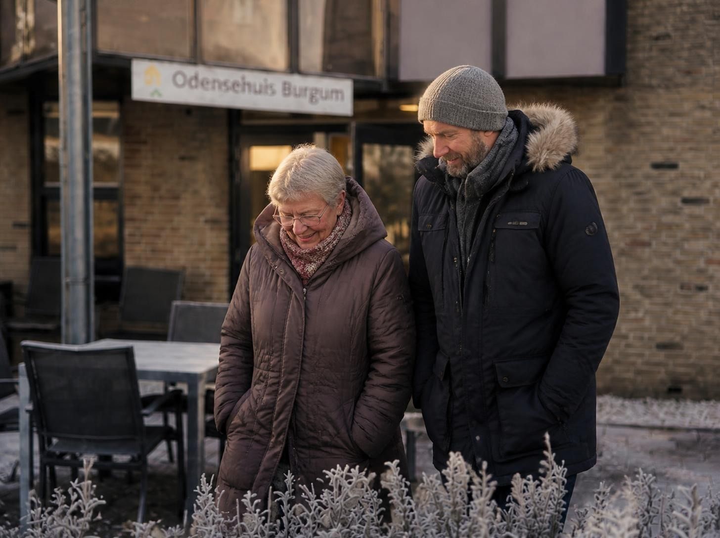 Een oudere vrouw en een jongere man lopen samen lachend naar de ingang van het Odensehuis Burgum